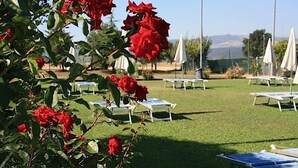A garden with red flowers and white lounge chairs. - Cascina Bosco Gerolo (Rivergaro)