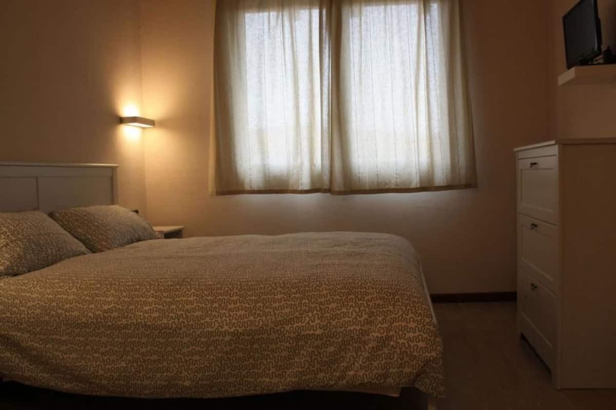 Een slaapkamer met een bed, nachtkastje, kast en een raam met gordijnen.