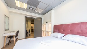 A hotel room with a large bed, a desk, and a chair. There is a door leading to another room. - Athens Welcome Suites Apartments (Athens)