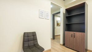 A modern interior with a dark upholstered chair, a wooden cabinet with open shelves, and two framed signs on the wall. - Athens Welcome Suites Apartments (Athens)