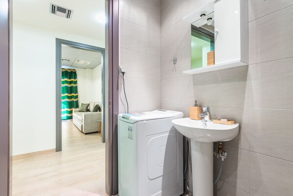 A modern bathroom with a washing machine, sink, and mirror.