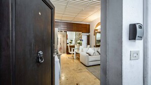 Un interior moderno con una puerta de madera oscura, un sofá blanco, una zona de comedor y una cocina visible a través de una puerta abierta.