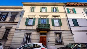 Un edificio con entrada central, varias ventanas con contraventanas y un pequeño balcón.