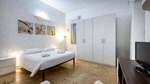 Un dormitorio con cama, mesita de noche, lámpara, armario y televisor.