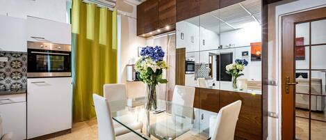 A modern kitchen with white cabinets, a stainless steel oven, and a glass dining table with white chairs.
