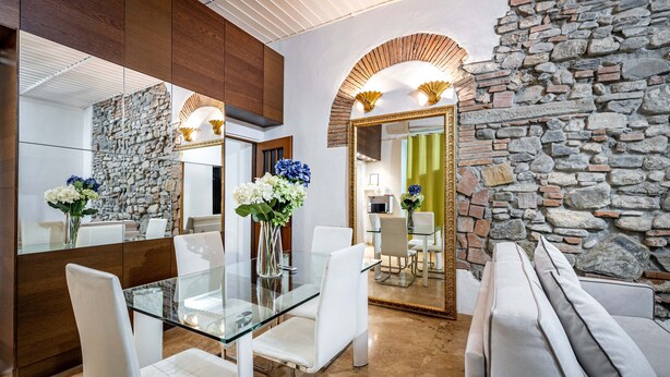 Un área de comedor moderna con una mesa de vidrio, sillas blancas y una pared de piedra.