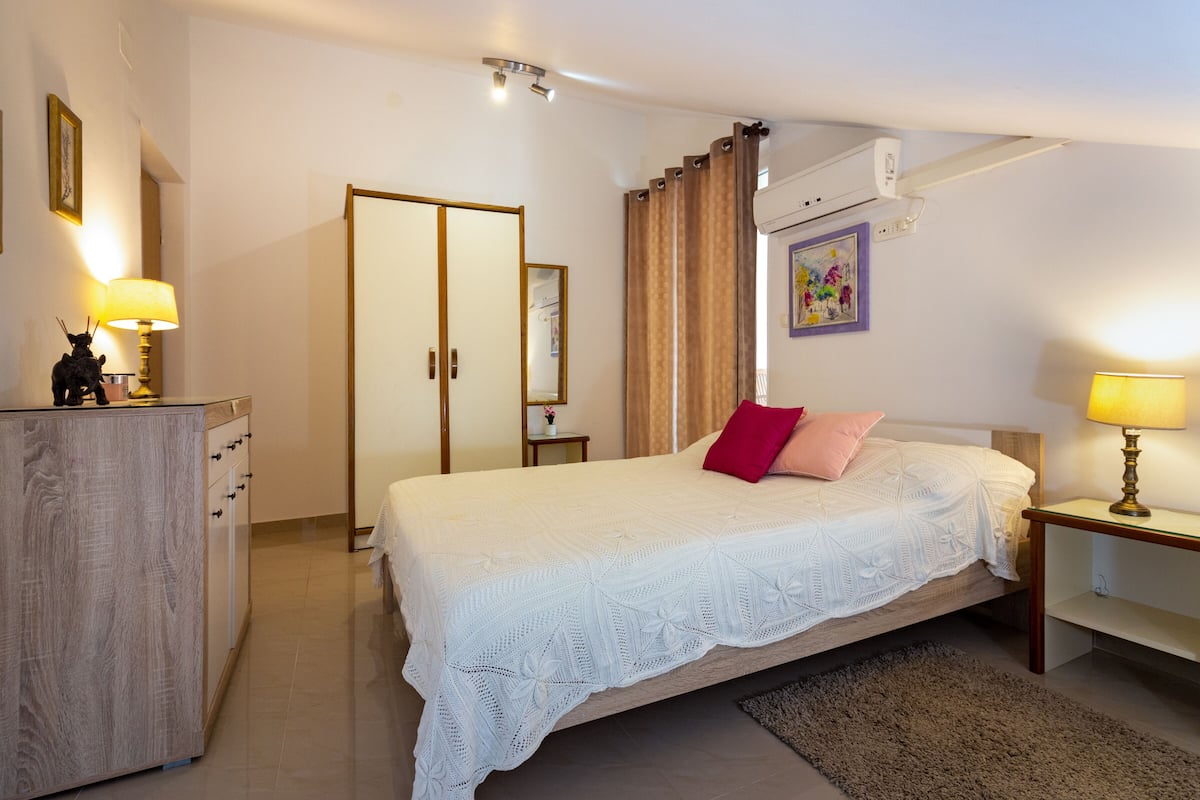 Quarto com cama, mesa de cabeceira, luminária, cômoda e espelho.