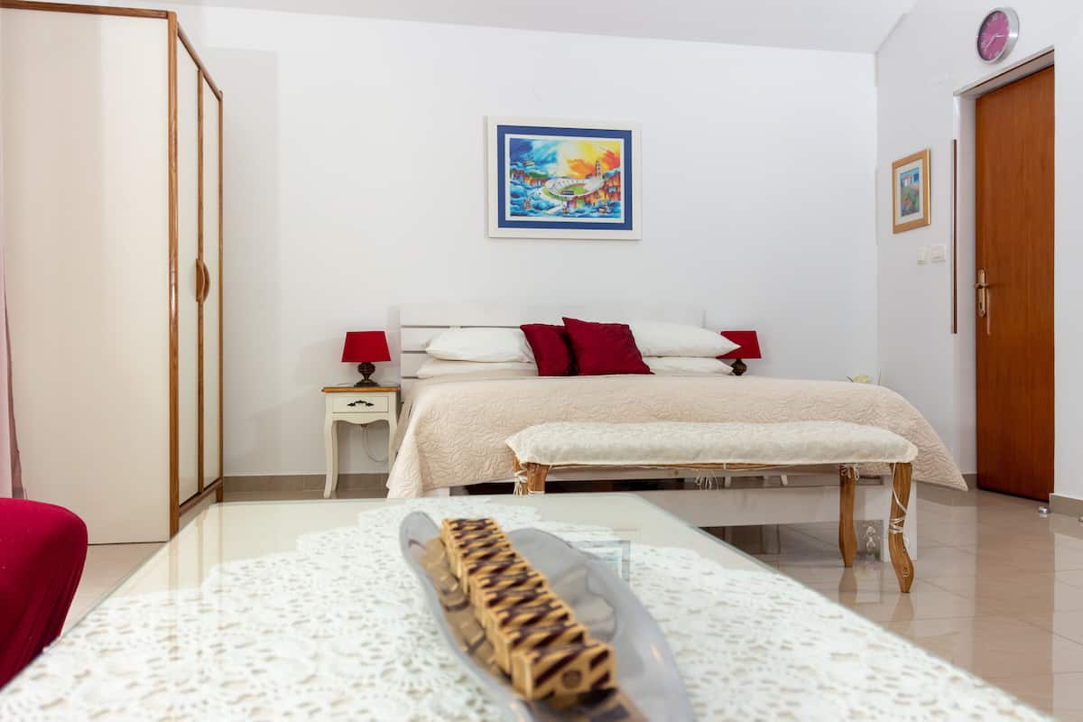 Quarto com cama, mesas de cabeceira, um banco e um quadro na parede.
