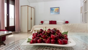 Ein Hotelzimmer mit einem Bett, einem Nachttisch mit einer Schale Kirschen, einem Glastisch und einem Kleiderschrank.