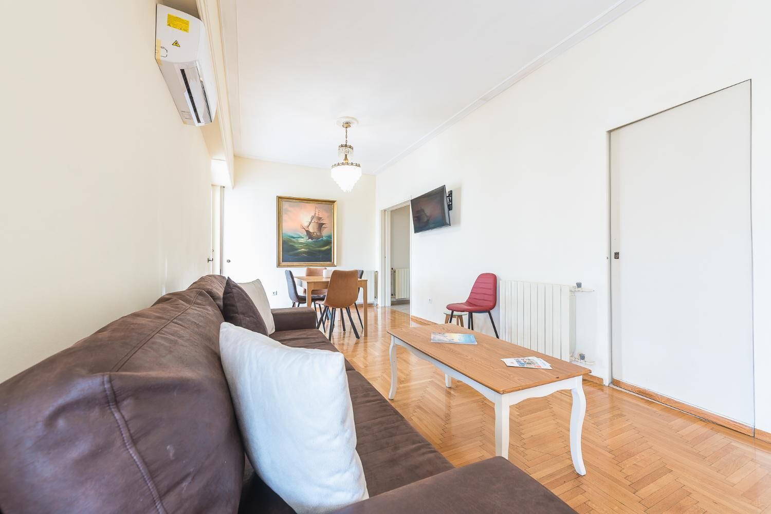 Uma sala de estar moderna com um sofá de couro marrom, uma mesa de centro de madeira e um espaço de jantar com mesa e cadeiras.