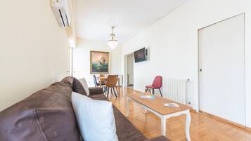 Uma sala de estar moderna com um sofá de couro marrom, uma mesa de centro de madeira e um espaço de jantar com mesa e cadeiras.