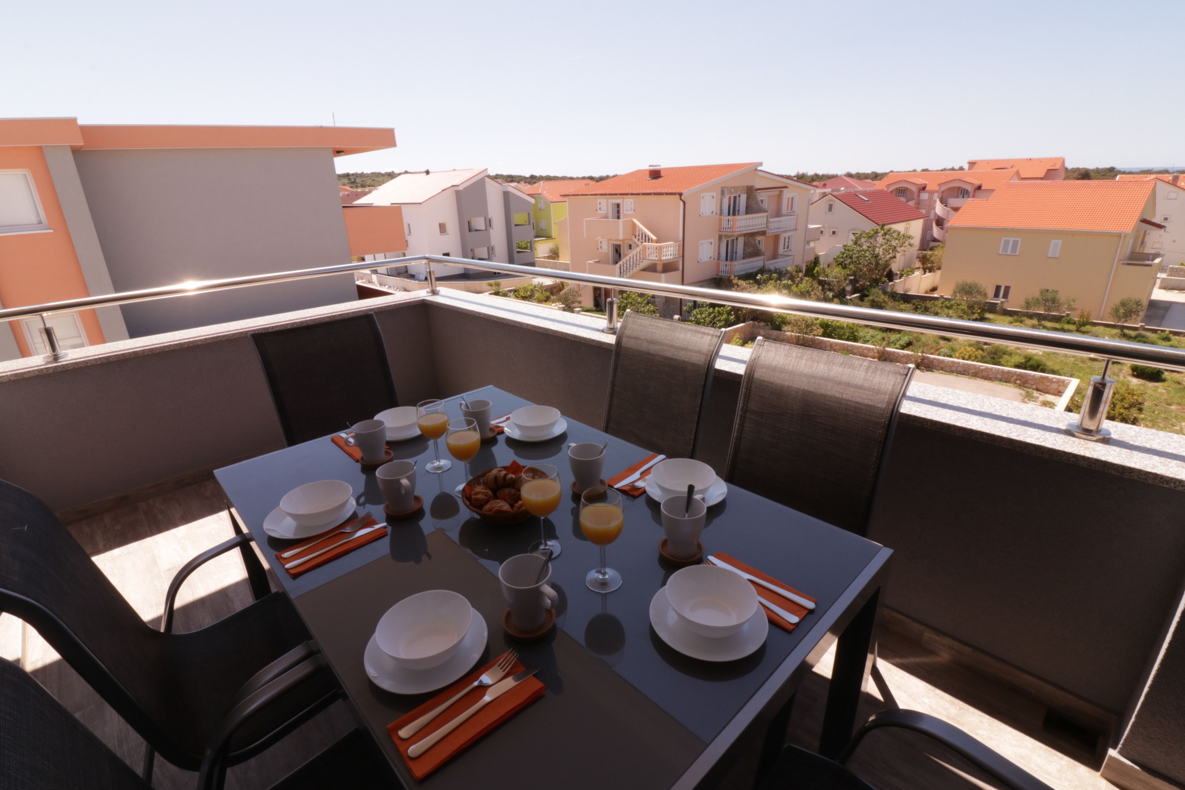 A balcony with a table set for breakfast, including plates, cups, and orange juice glasses.