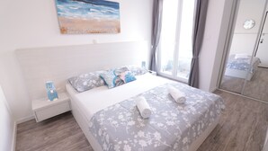 Ein Schlafzimmer mit Bett, Nachttisch, einem Gemälde und einem Fenster mit Vorhängen.