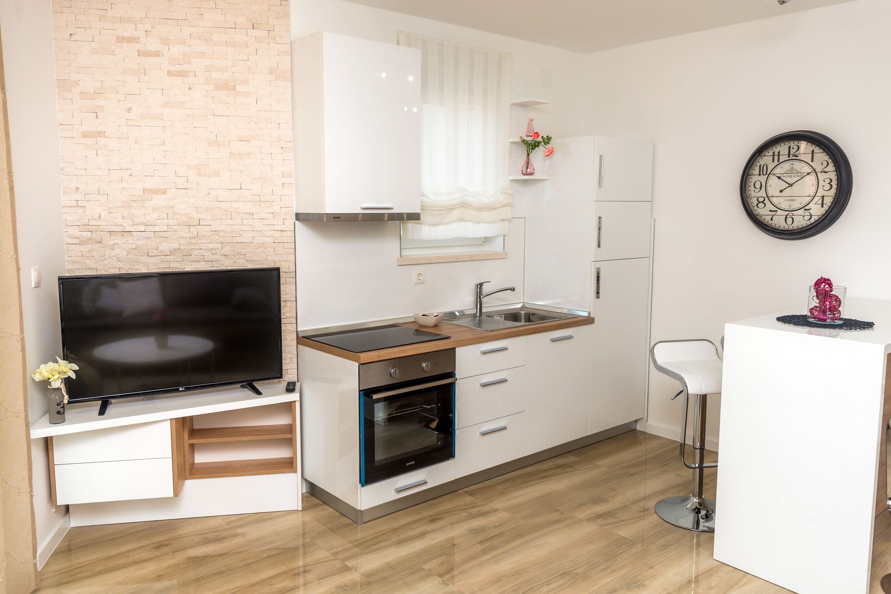 A modern kitchen with a TV, oven, sink, and bar stool.