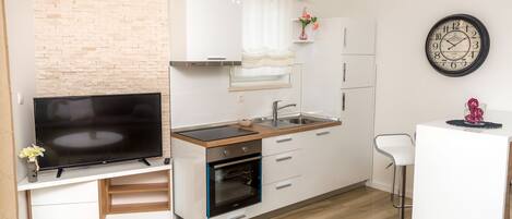 A modern kitchen with a TV, oven, sink, and bar stool.