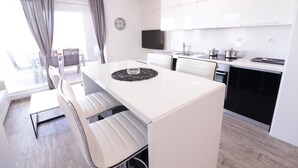 Eine moderne Küche mit weißen Schränken, ein Essbereich mit weißem Tisch und Stühlen sowie ein großes Fenster mit Vorhängen.