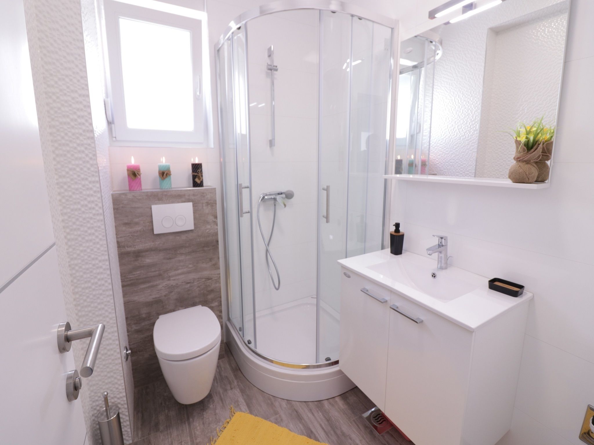 Ein modernes Badezimmer mit einer Duschkabine, einer weißen Toilette und einem Waschtisch mit Spiegel.