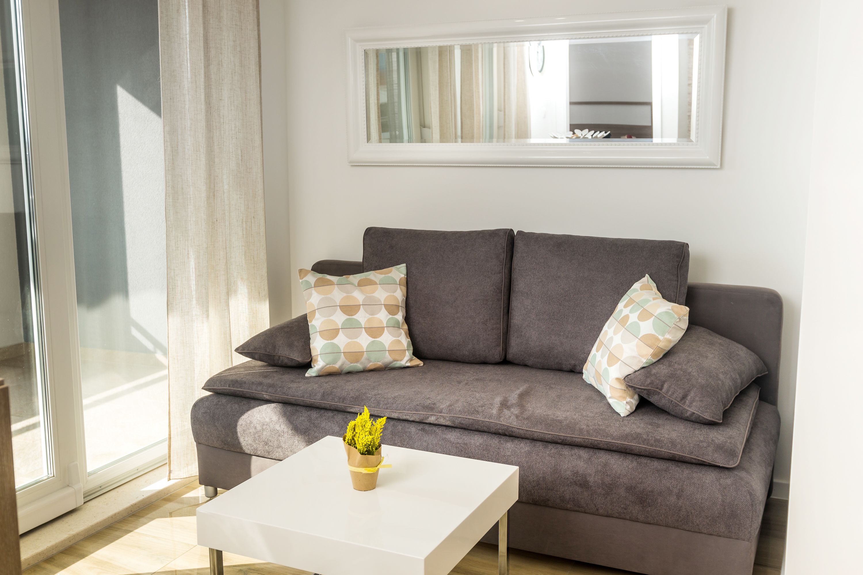 A modern living room with a grey sofa, two patterned pillows, a white coffee table, and a small potted plant.