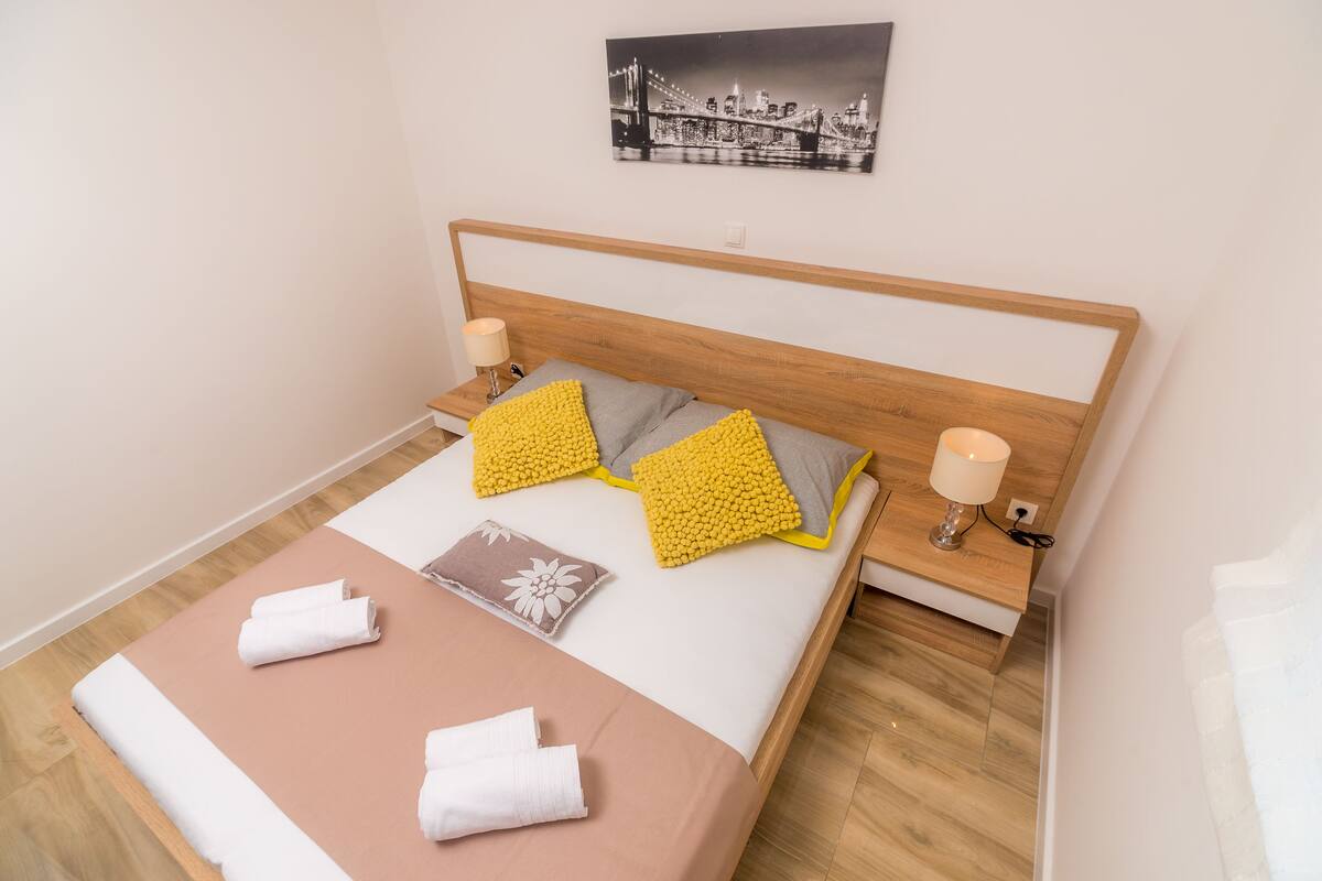 A neatly made bed with a wooden headboard, two bedside lamps, and a cityscape artwork on the wall.