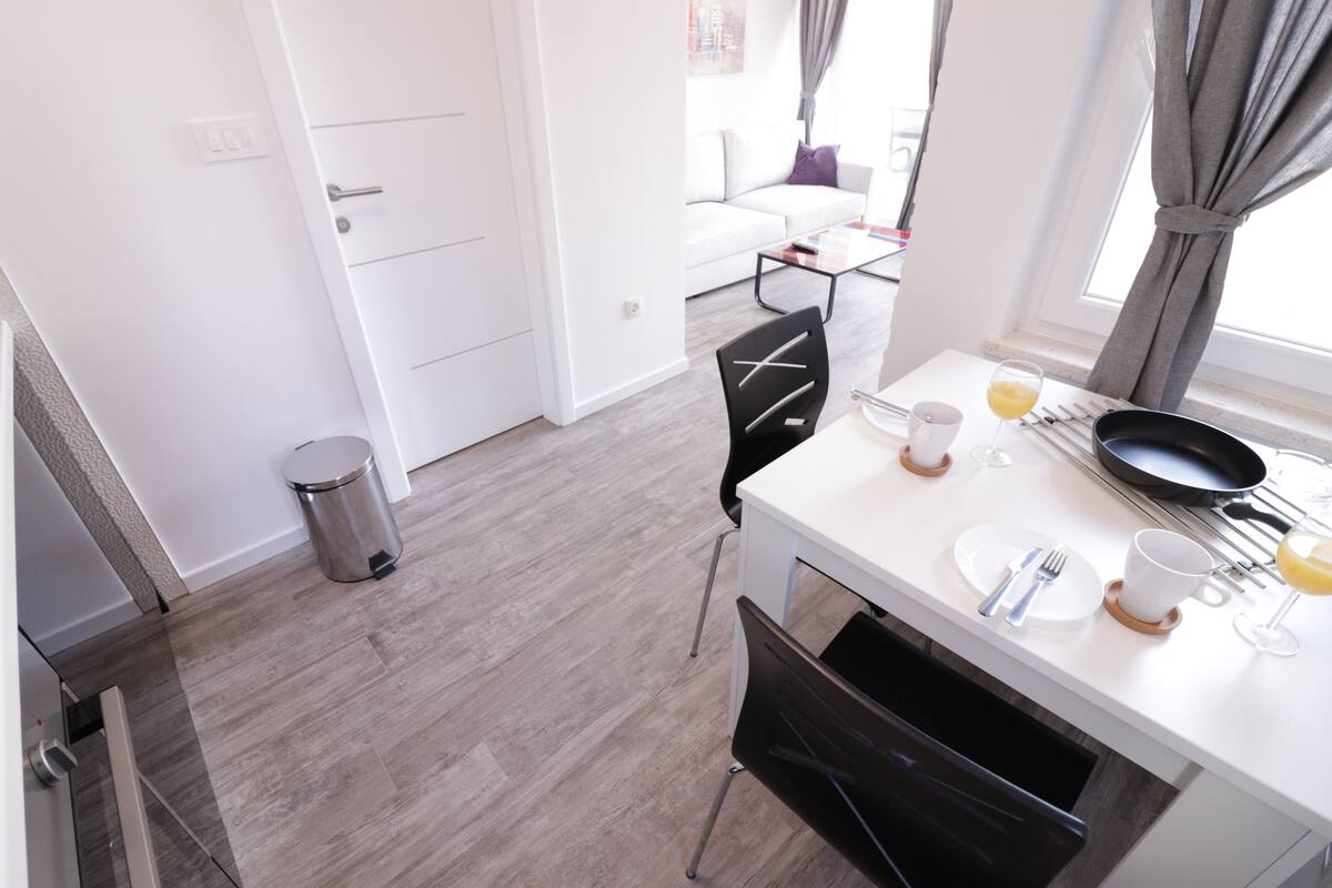 A modern kitchen with a white countertop, a black chair, and a dining table set with plates, cups, and cutlery.