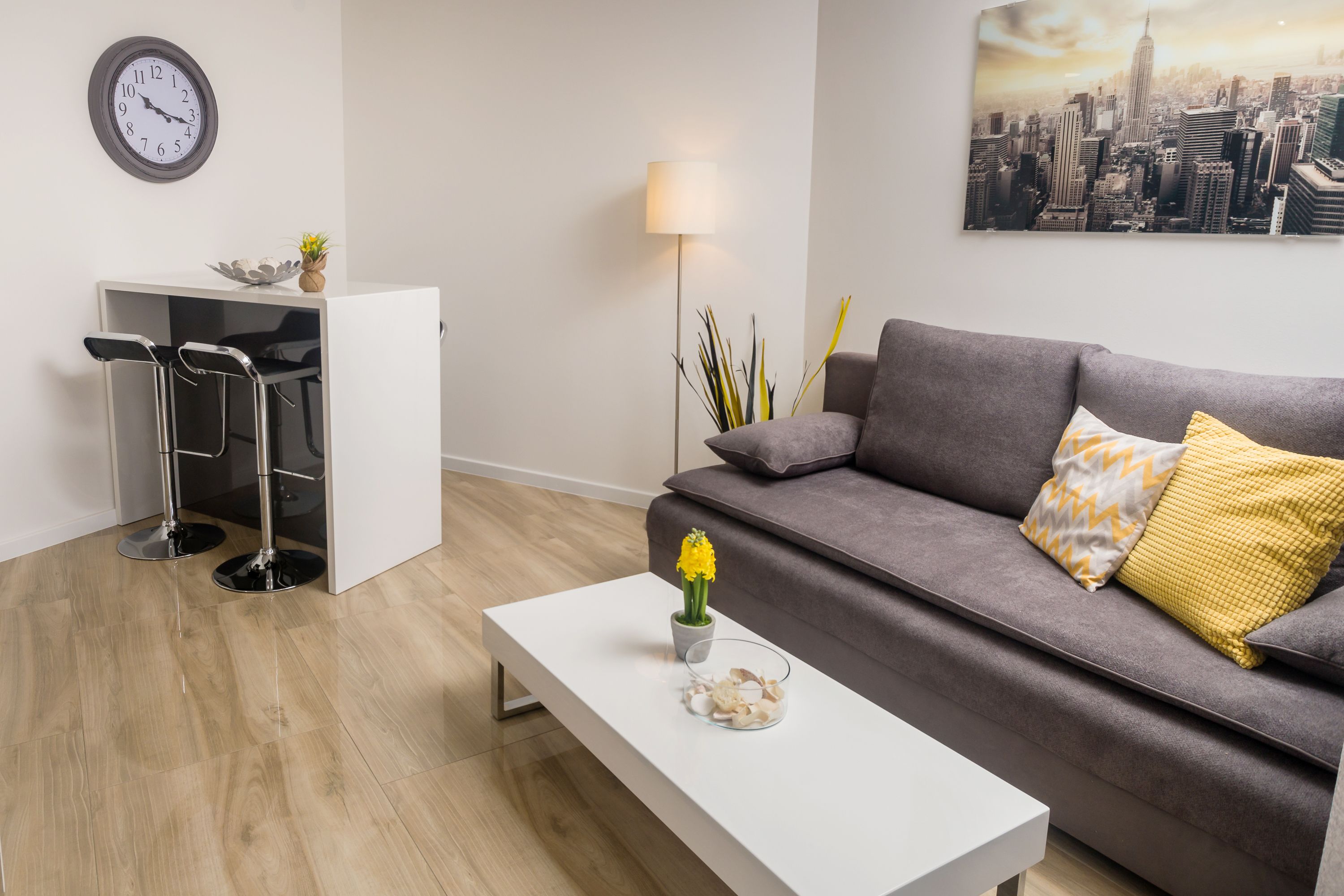 A modern living room with a grey sofa, a white coffee table, and a cityscape painting on the wall.