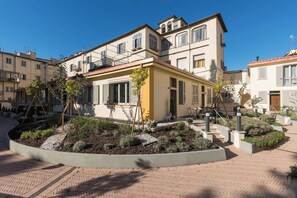 A residential building with a central entrance, a small garden area, and a paved walkway.