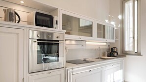 Una cocina moderna con armarios blancos, horno integrado, microondas y cafetera.