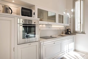 Una cucina moderna con mobili bianchi, forno ventilato, microonde e macchina per il caffè.