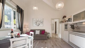 Una cocina moderna con armarios blancos, un comedor con mesa y sillas blancas, y una sala de estar con sofá y un cuadro en la pared.