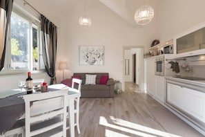 Una cucina moderna con mobili bianchi, un'area pranzo con tavolo e sedie bianche, e un soggiorno con divano e un quadro appeso al muro.