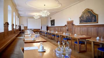Une salle de conférence avec de longues tables, des chaises bleues, un écran de projection et un lustre.