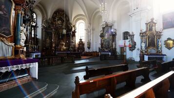 An interior of a church with ornate altars, wooden pews, and a high arched ceiling.
