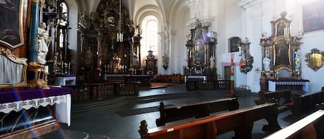 Ein Kircheninneres mit aufwendig verzierten Altären, Holzbänken und einer hohen, gewölbten Decke.