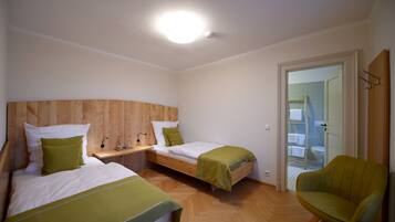 A bedroom with two beds, a wooden headboard, a green chair, and a bathroom visible through an open door.