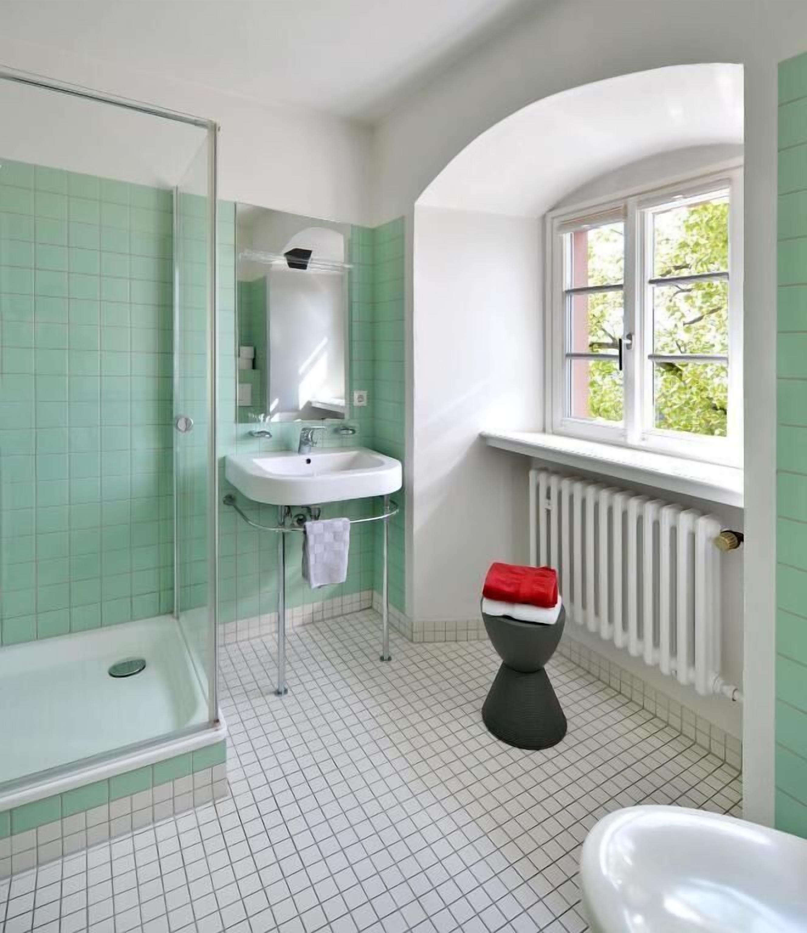A bathroom with a shower, sink, toilet, and a window with a view of greenery.