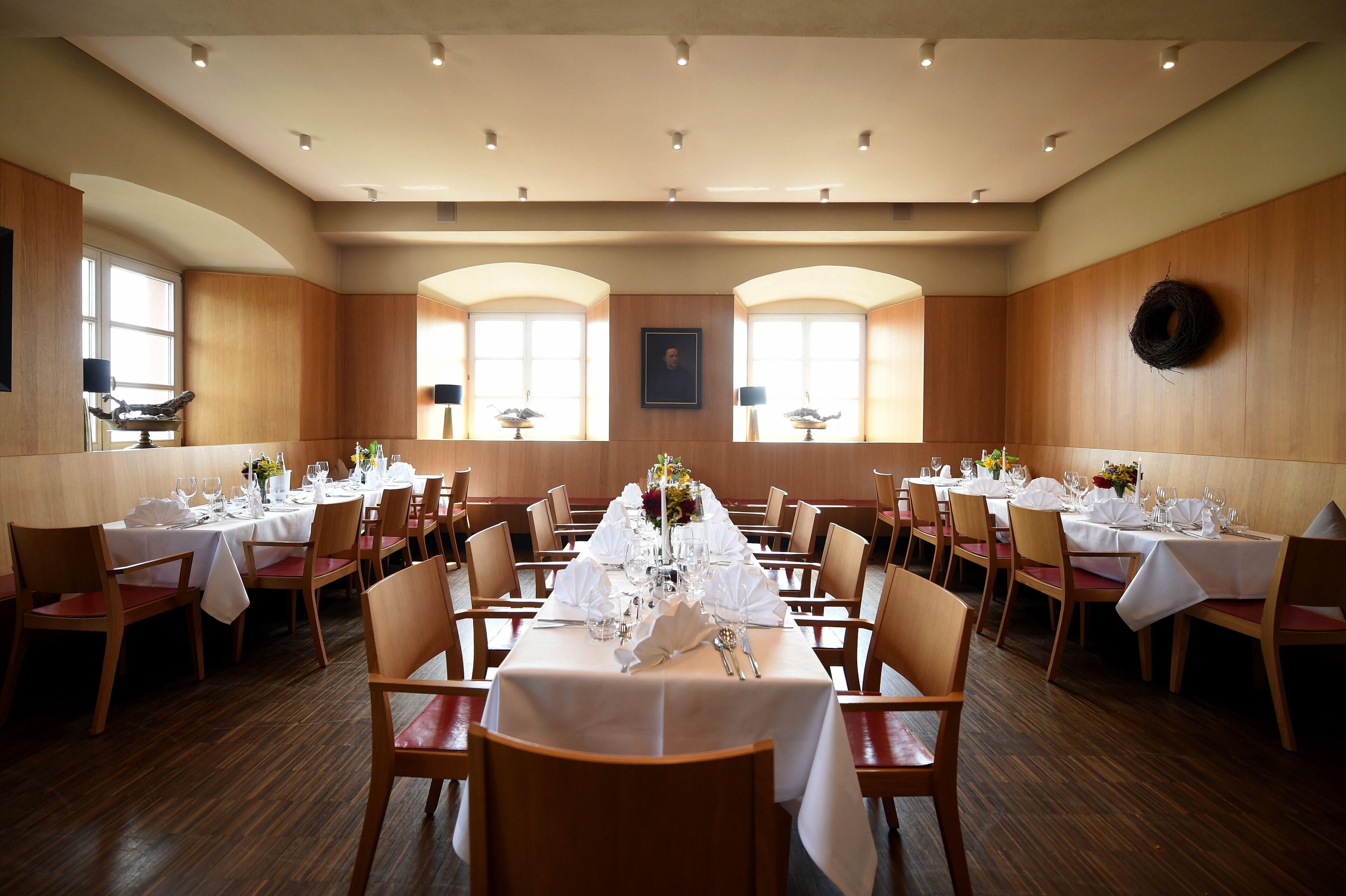 Une salle à manger avec plusieurs tables dressées pour un événement formel, agrémentée de nappes blanches, de chaises et de centres de table.