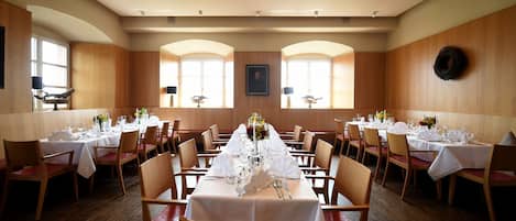 A dining area with multiple tables set for a formal event, featuring white tablecloths, chairs, and centerpieces.