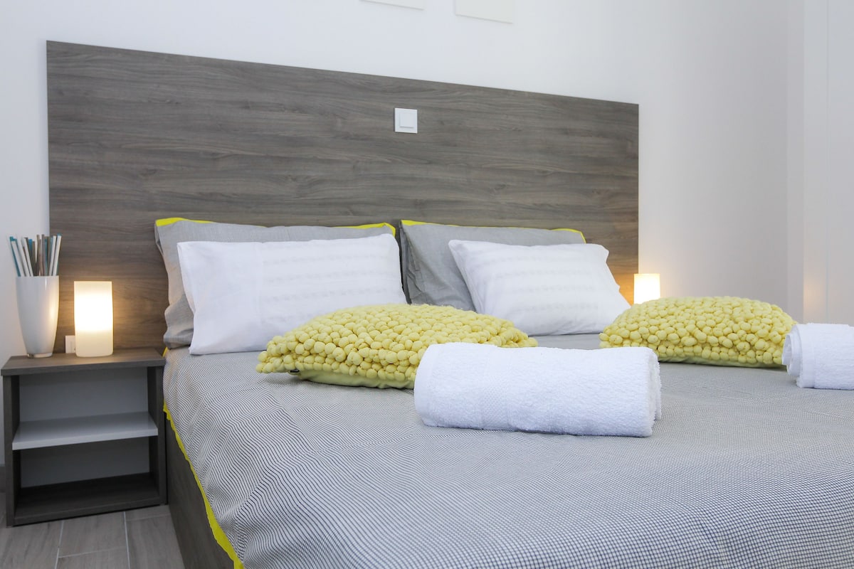 A neatly made bed with a grey and white striped bedspread, two pillows, and two rolled towels.