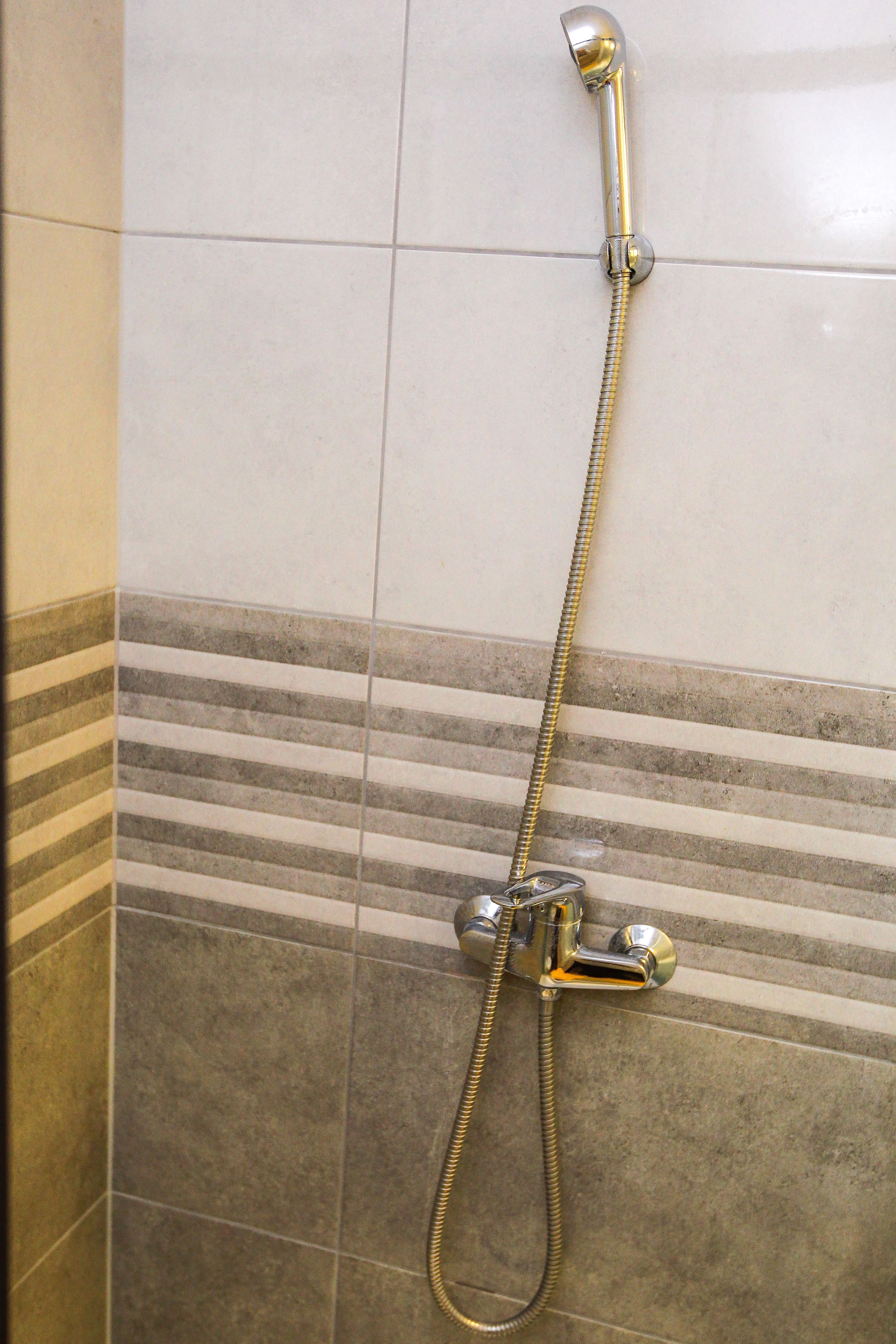Ducha con manguera de mano y cabezal de ducha empotrado en una pared revestida de azulejos con diseño a rayas.