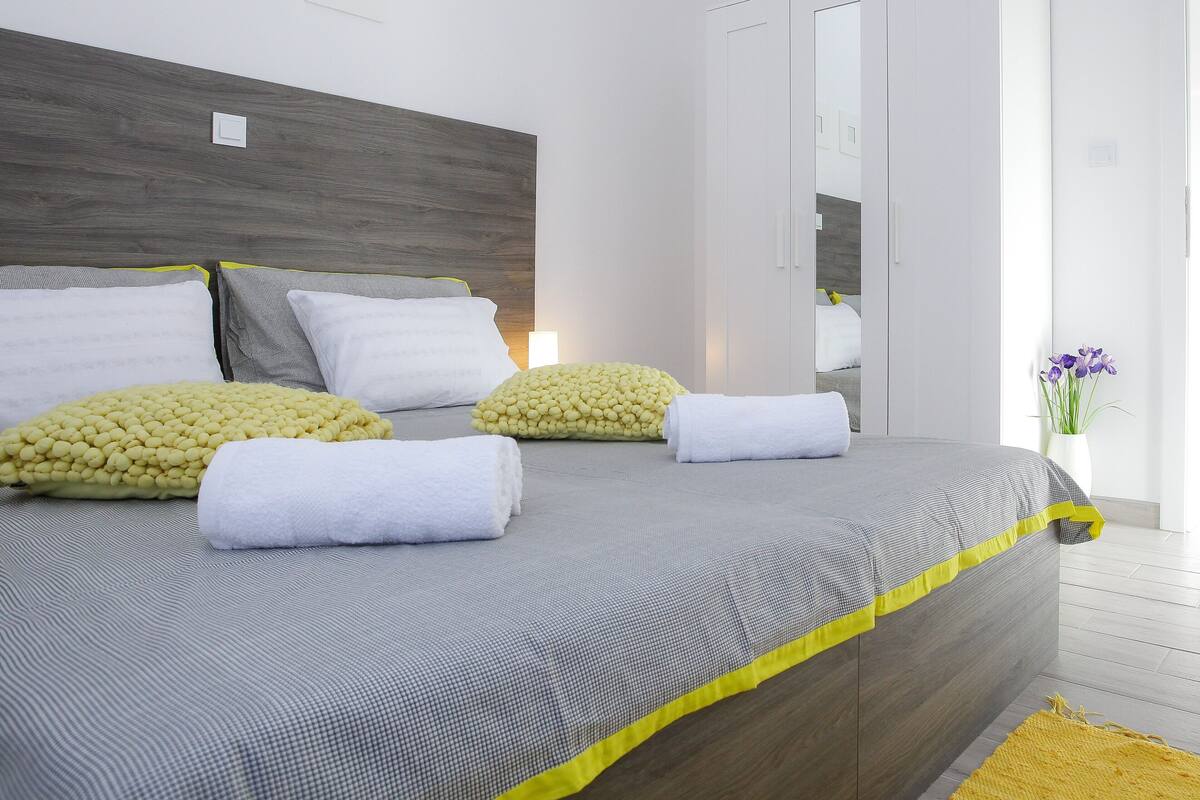 A modern bedroom with a large bed, a wardrobe, and a small table with a vase.