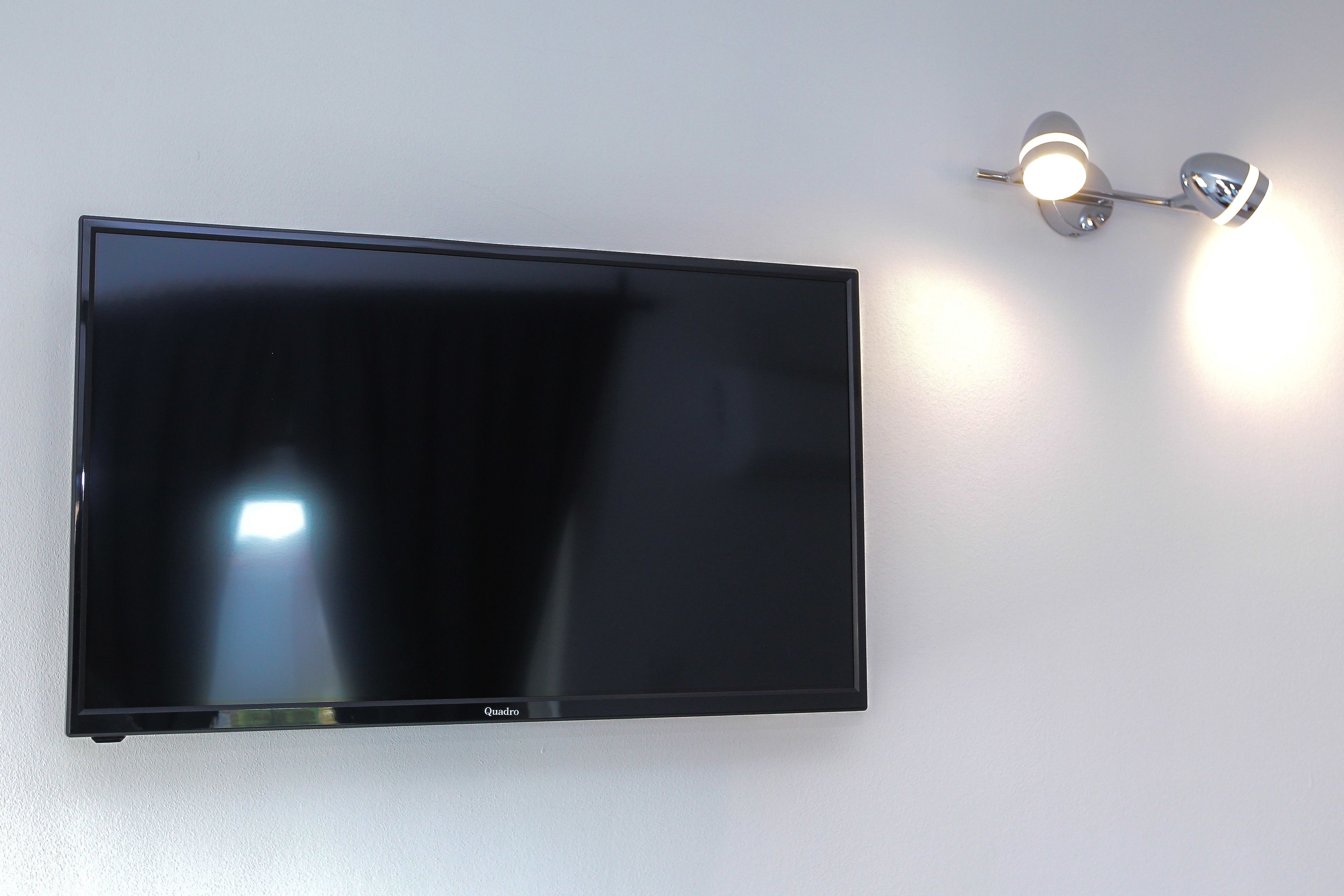 Ein Flachbildfernseher an der Wand, daneben eine wandmontierte Leuchte.
