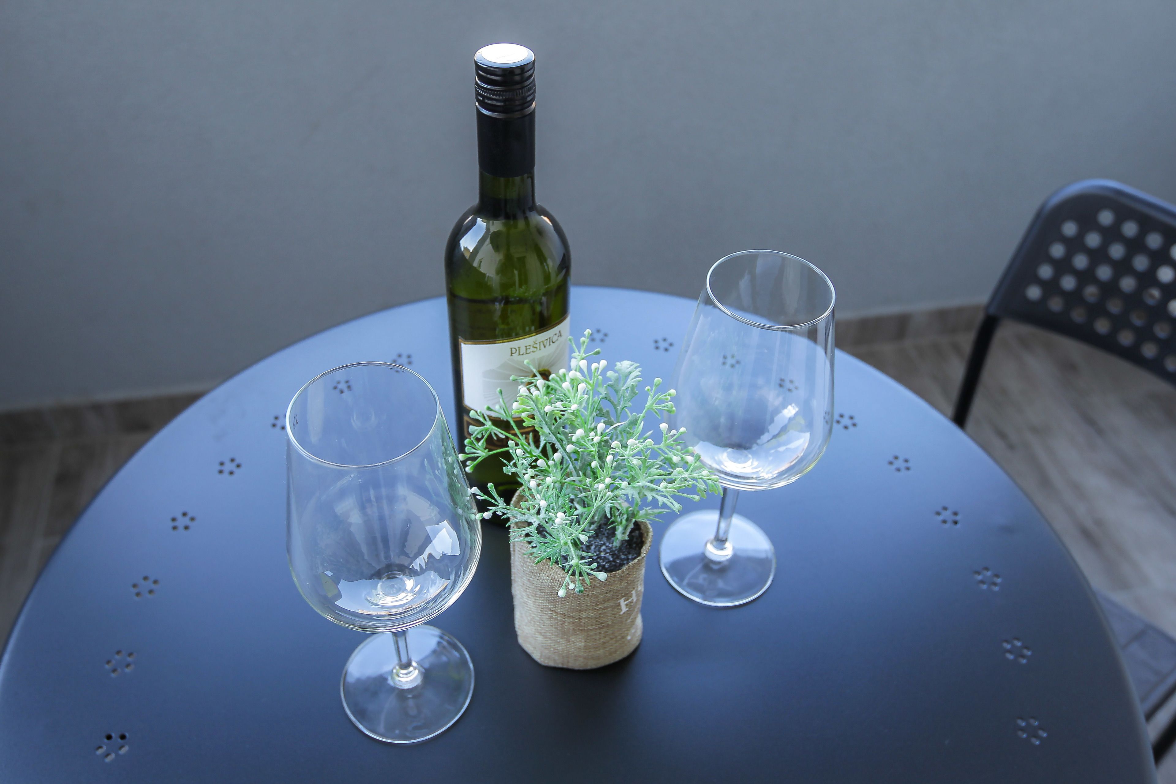 A bottle of Plessivica wine, two empty wine glasses, and a small potted plant on a round table.
