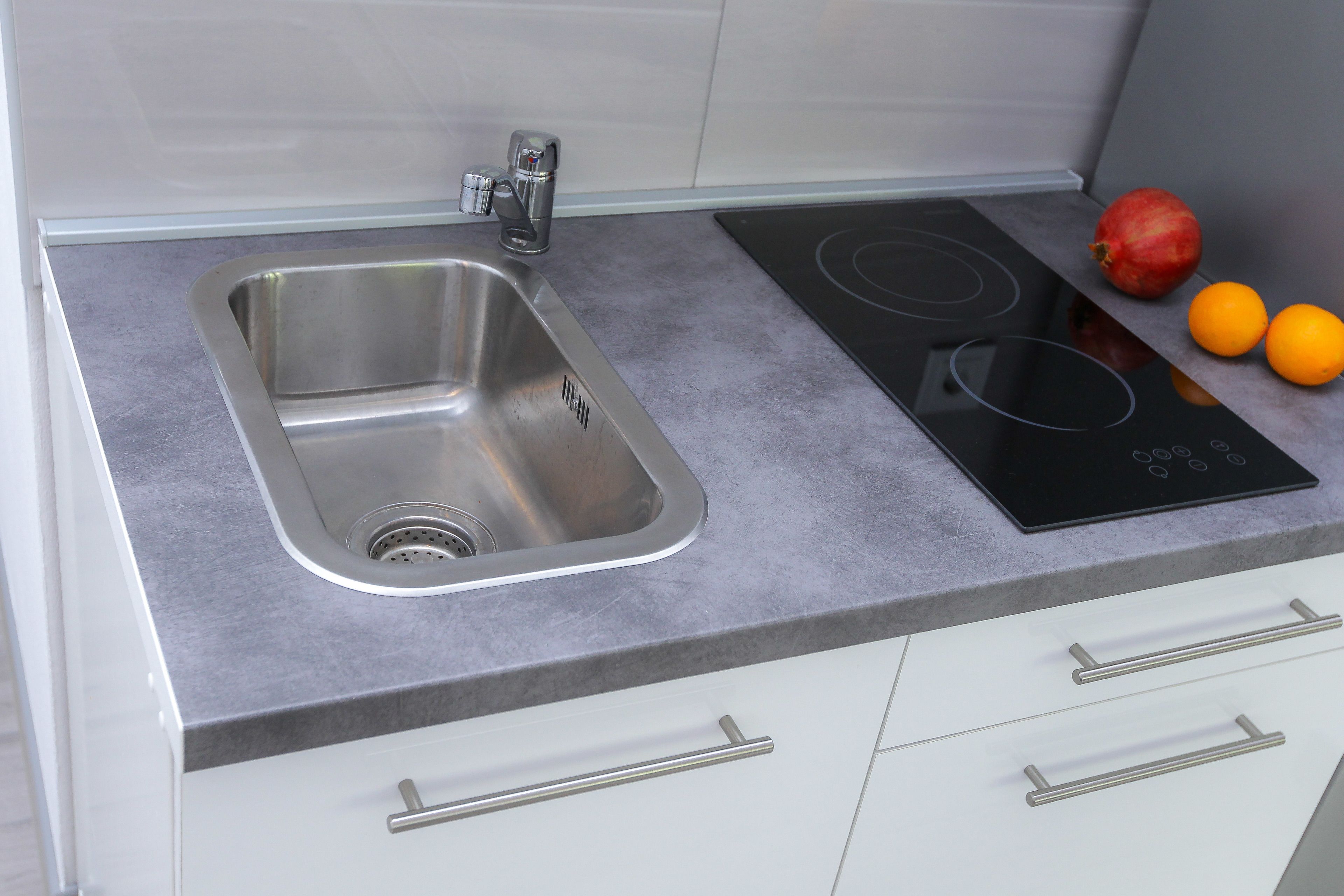 A kitchen with a stainless steel sink, a black induction cooktop, and two oranges on the counter.
