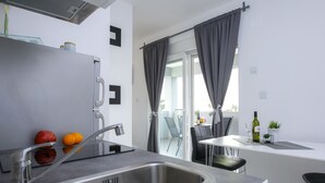 A modern kitchen with a stainless steel sink, a dining area with a table and chairs, and a balcony with curtains. - Pool Apartments Privilege (Novalja)