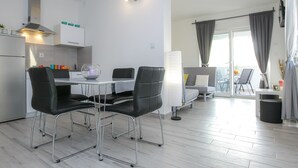 A modern kitchen with a dining area, a balcony with curtains, and a view of the city. - Pool Apartments Privilege (Novalja)