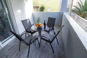 A balcony with a round table, four chairs, a bowl of fruit, a bottle of wine, and a glass.