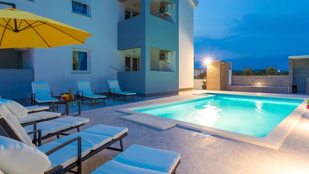 A modern building with a swimming pool, sun loungers, and a yellow umbrella. - Pool Apartments Privilege (Novalja)