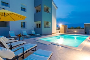 A modern building with a swimming pool, sun loungers, and a yellow umbrella.