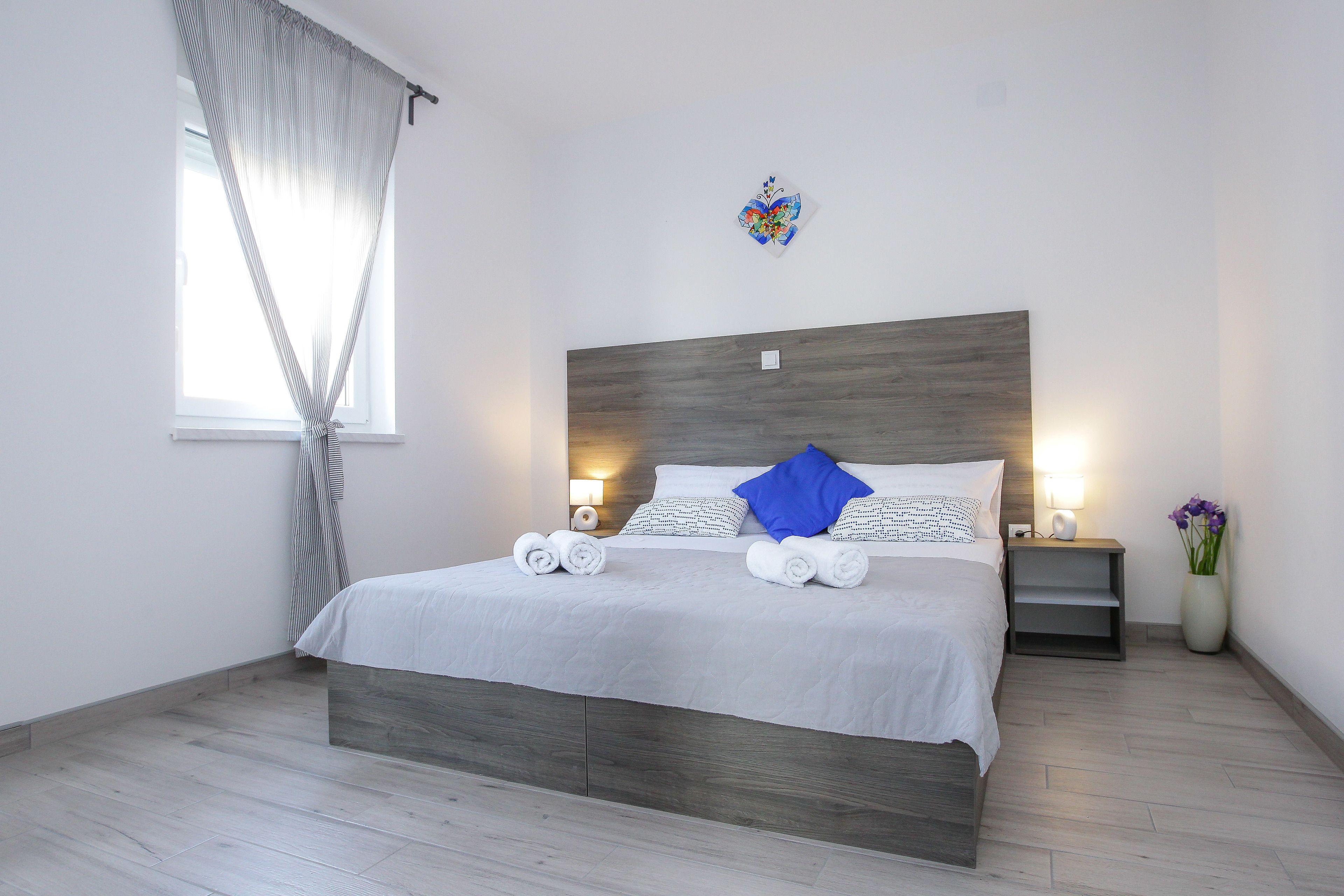 A neatly made bed with white linens and rolled towels, a bedside table with a lamp, and a wall-mounted artwork.