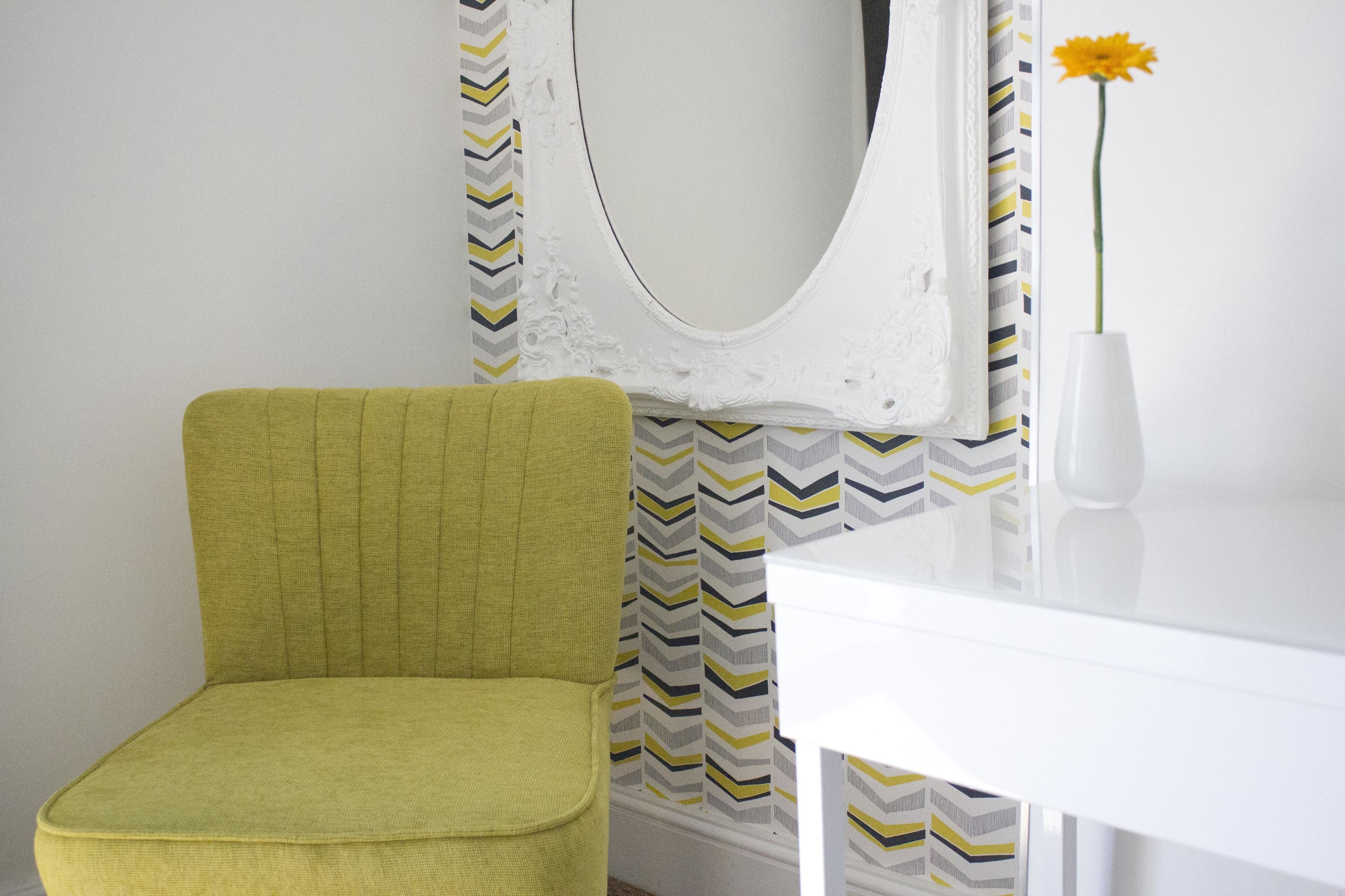 A room with a green chair, a white table, and a mirror with a chevron-patterned curtain.